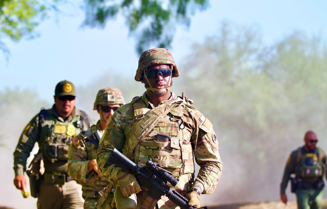 A guardsman walks ahead of another guardsman and other law enforcement officials during the day.