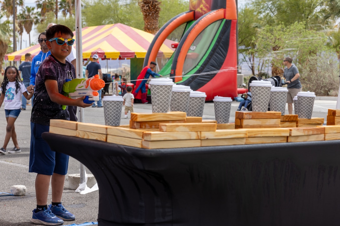 A child knocks over cups with a water gun during the 2025 Superfest at Marine Corps Air Ground Combat Center, Twentynine Palms, California, April 12, 2025. Superfest and other Marine Corps Community Services events are hosted annually in honor of the month of the military child, supporting and enhancing the quality of life for the service members, Department of Defense civilians, and families of The Combat Center. (U.S. Marine Corps photo by Cpl. Anna Higman)