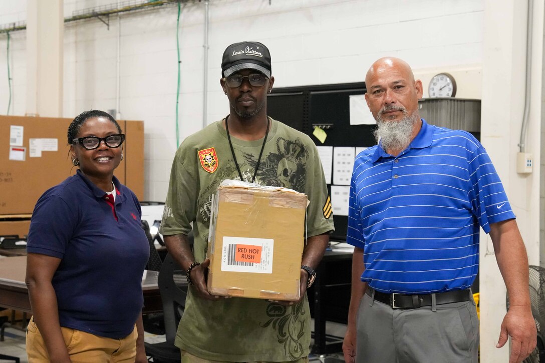 Three people stand for a photo holding a box