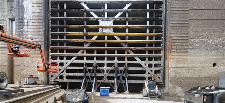 a lock gate rests on four hydraulic jacks with construction equipment nearby.