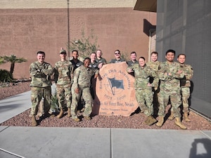 Airmen stand in a group for a photo around a statue emblazoned with the Red Flag logo.