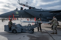 U.S. Air Force Senior Airman Devon Kramm, left, a 57th Aircraft Maintenance Squadron (AMXS) load crew member, operates a jammer as Staff Sgt. Madison Andrews, center, a 57th AMXS crew chief, and Senior Airman Scott Demar, right, a 57th AMXS load crew member, steady the munitions during the first quarter weapons standardization load crew competition at Nellis Air Force Base, Nevada, April 18, 2025.