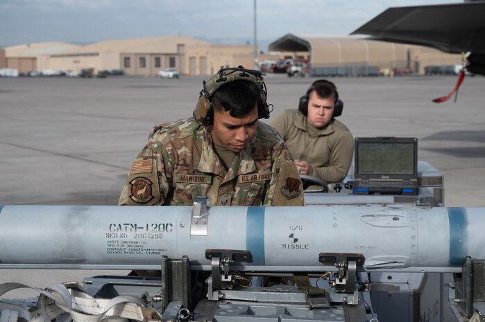 U.S. Air Force Staff Sgt. Mark Anthony Mangune, a 57th Aircraft Maintenance Squadron (AMXS) crew chief, checks a missile before loading it as Senior Airman Brighton Robinson, a 57th AMXS load crew member, operates a jammer during the first quarter weapons standardization load crew competition at Nellis Air Force Base, Nevada, April 18, 2025