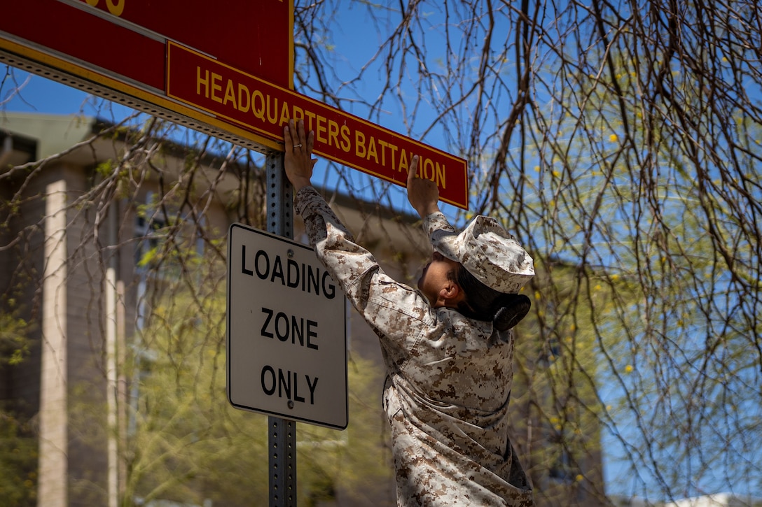 U.S. Marine Corps Staff Sgt. Amber Kelly, a Colorado native, facilities chief with Headquarters Battalion, Marine Air Ground Task Force Training Command, Marine Corps Air Ground Combat Center, attaches the Headquarters Battalion sign to the bachelor enlisted quarters sign at building 1608, MCAGCC, Twentynine Palms, California, April 10, 2025. Operation Clean Sweep is a Marine Corps initiative to ensure enlisted Marines have clean, healthy and safe living conditions. (U.S. Marine Corps photo by Cpl. Iris Gantt)