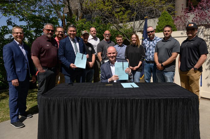 Utah Gov. Spencer Cox holds up the signed S.B. 17 during a visit to Hill Air Force Base, Utah, with DoD civilian employees standing behind him.