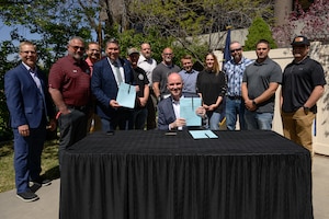 Utah Gov. Spencer Cox holds up the signed S.B. 17 during a visit to Hill Air Force Base, Utah, with DoD civilian employees standing behind him.