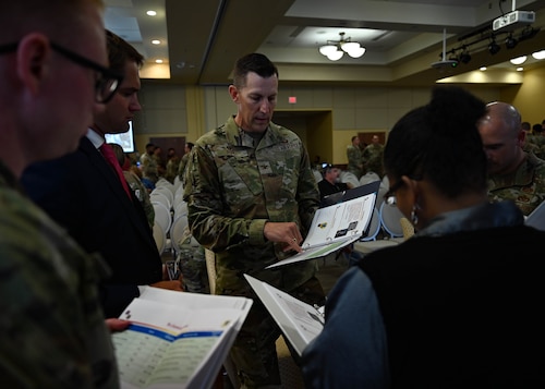 Judging panel stands in a group, holding binders, discussing and selecting the winning idea during Keesler AFB’s Dragon Tank event.