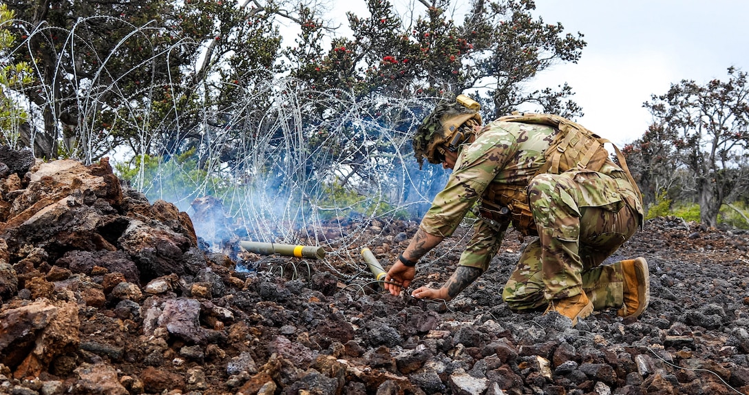 A Soldier is next to barbwire on setting up explosive charges to remove the obstructing wire.