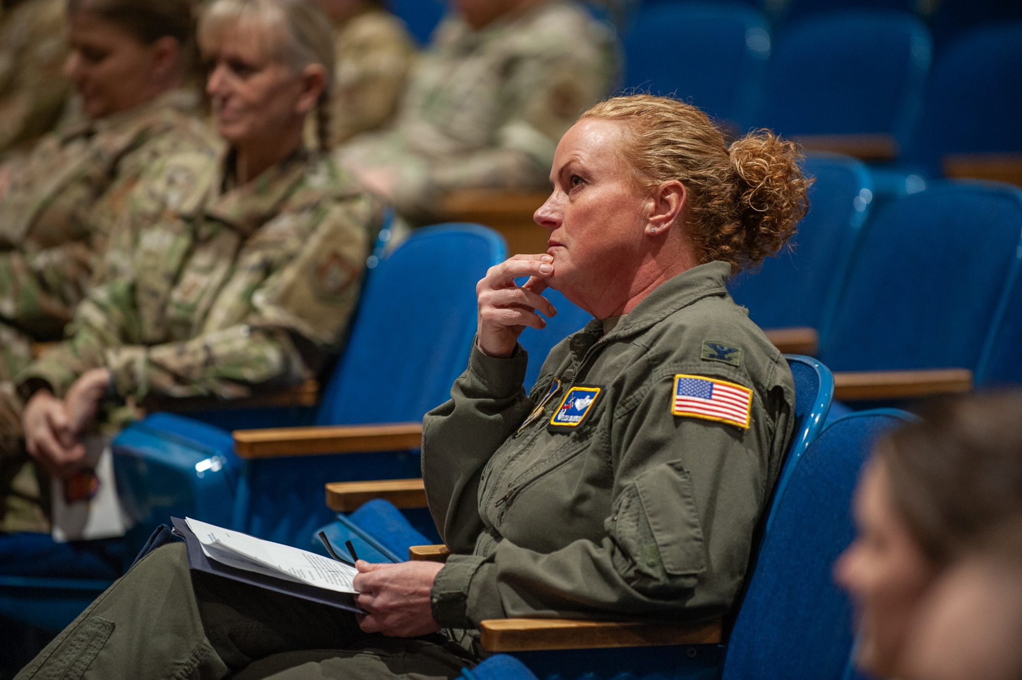 A woman in a flight suit sits in theater seating.