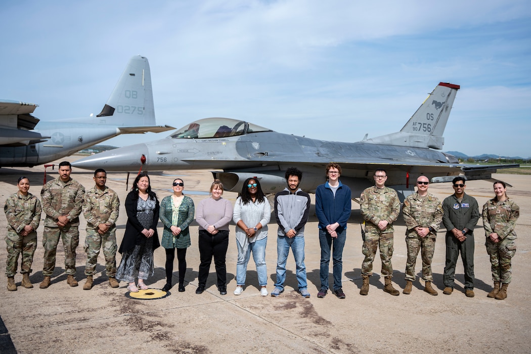People stand in front of a jet and pose for a photo.
