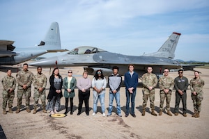 People stand in front of a jet and pose for a photo.