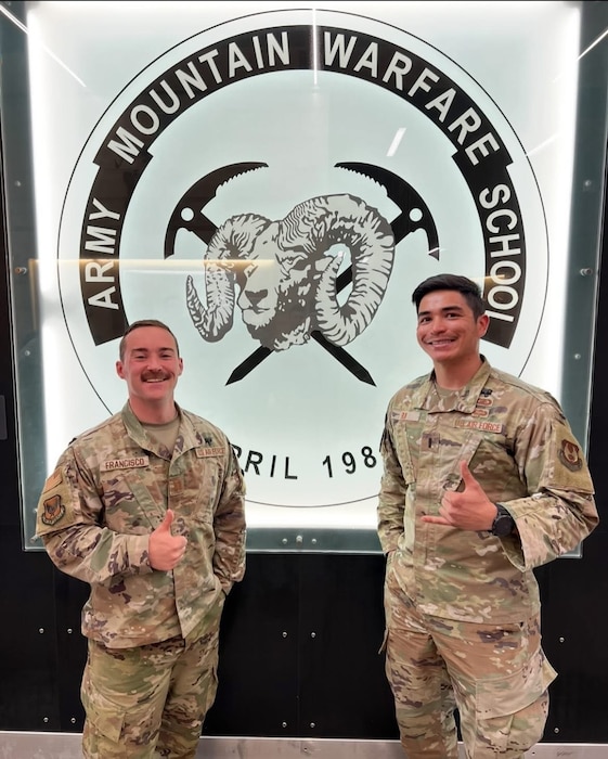 Two Airmen stand in front of school logo