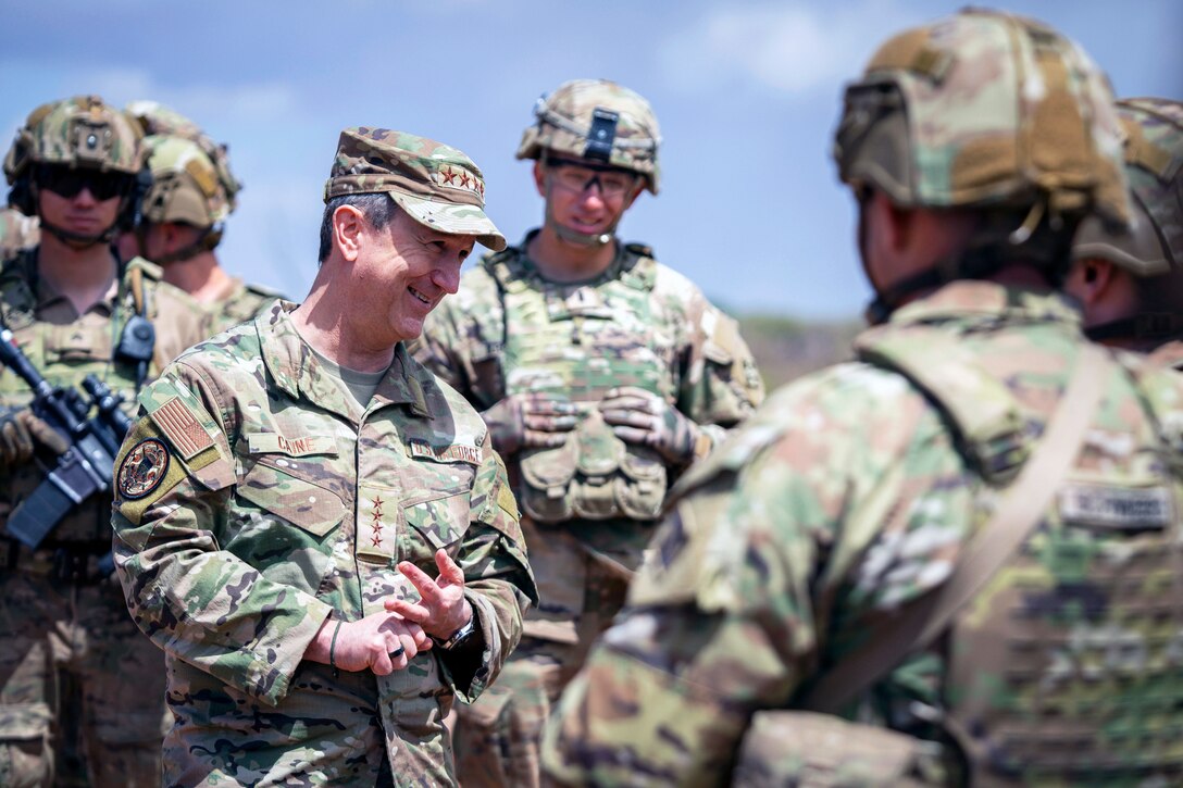 A military leader wearing camo speaks with soldiers while standing outside during the day.