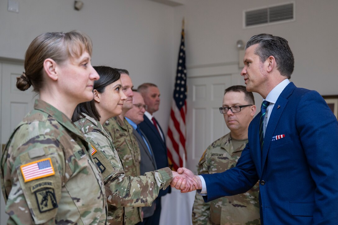 The defense secretary shakes hands with a service member as fellow service members stand nearby.
