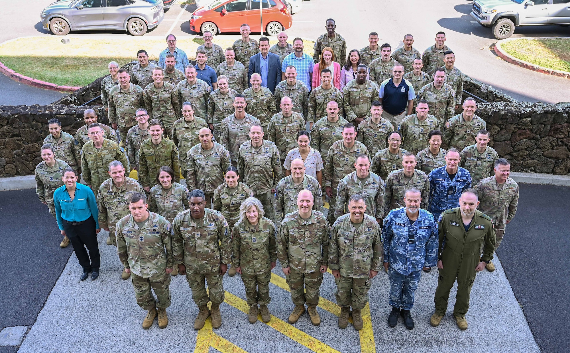Over 60 people stand together in a group and look up at the camera for a group photo.