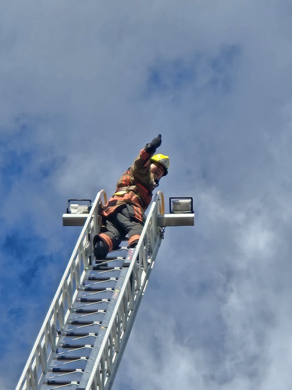 Man on top of fire ladder giving thumbs up sign.