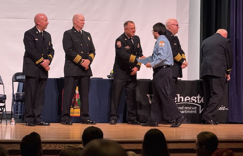 Man accepts certificate and shakes the hand of man in fire uniform.