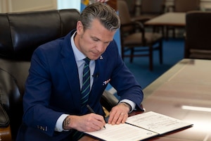 The defense secretary signs a document in an office.