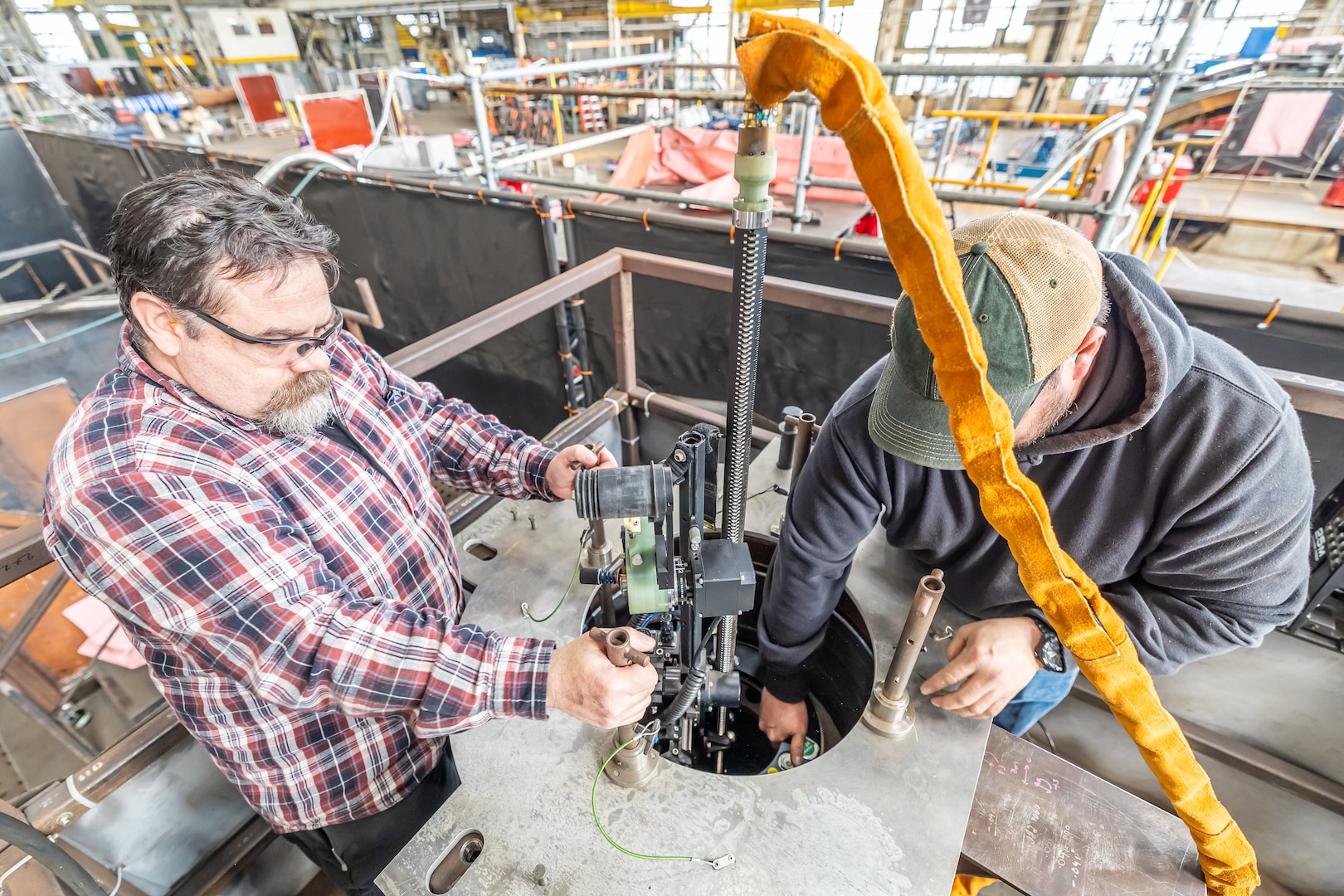 Josh Maya (left), Waterfront Support and welding work lead, Code 100TO.3, Moonshine Lab; and Bryan Hara (right), Welding Instructor, Advanced Continuous Training Development, Shop 26 lower an Encompass Welding Machine in a Rudder Bore mock-up April 9, 2025, at Puget Sound Naval Shipyard & Intermediate Maintenance Facility in Bremerton, Washington. (U.S. Navy photo by Jeb Fach)