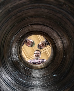 Bryan Hara (top left), welding instructor, Advanced Continuous Training Development, Shop 26; Josh Maya (center), Waterfront Support and welding work lead, Code 100TO.3, Moonshine Lab; and Josh Hughes (top right), welder training leader, Shop 26, pose for a photograph at the top of a rudder bore mockup in Building 460  April 9, 2025, at Puget Sound Naval Shipyard & Intermediate Maintenance Facility in Bremerton, Washington. The mock-up is used for training welders in rudder bore repair. (U.S. Navy photo by Jeb Fach)