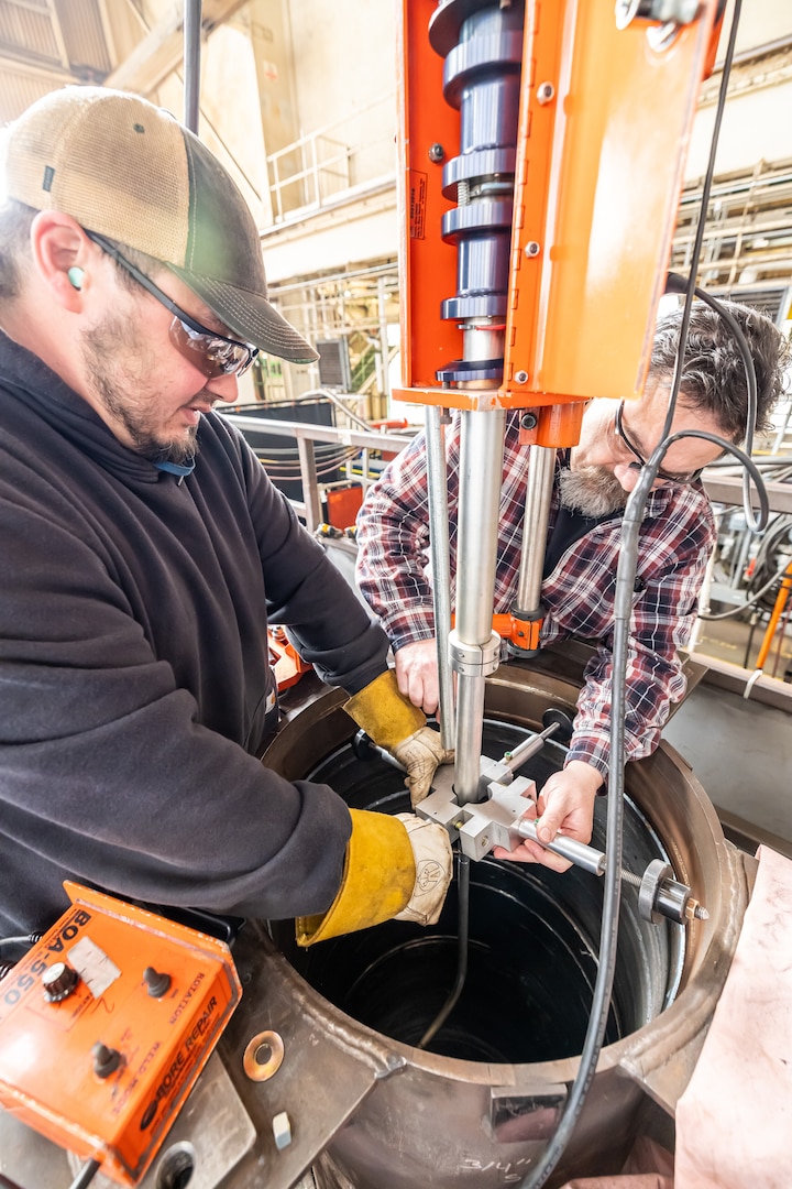 Josh Maya and Bryan Hara lower the Encompass Welding Machine into the Rudder Bore mock-up in Building 460, April 9, 2025, at Puget Sound Naval Shipyard & Intermediate Maintenance Facility in Bremerton, Washington. (U.S. Navy photo by Jeb Fach)