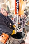 Josh Maya and Bryan Hara lower the Encompass Welding Machine into the Rudder Bore mock-up in Building 460, April 9, 2025, at Puget Sound Naval Shipyard & Intermediate Maintenance Facility in Bremerton, Washington. (U.S. Navy photo by Jeb Fach)
