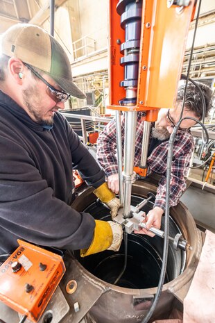 Josh Maya and Bryan Hara lower the Encompass Welding Machine into the Rudder Bore mock-up in Building 460, April 9, 2025, at Puget Sound Naval Shipyard & Intermediate Maintenance Facility in Bremerton, Washington. (U.S. Navy photo by Jeb Fach)