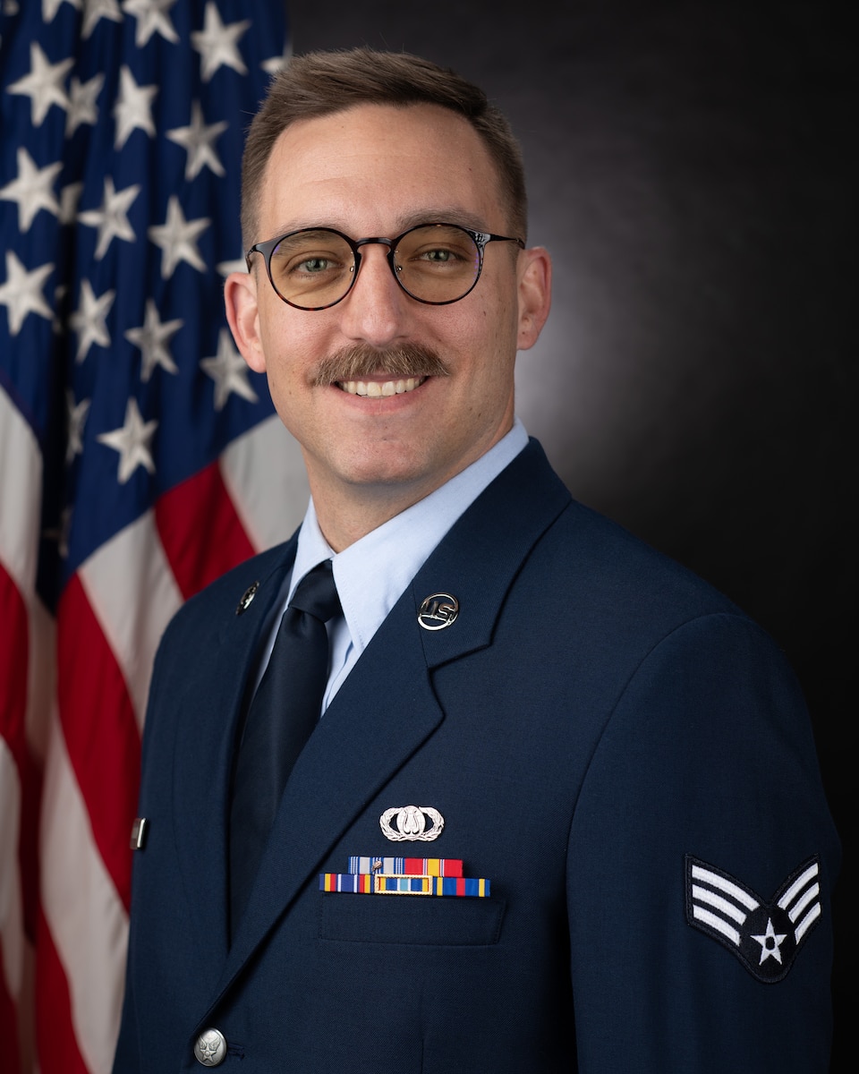 Official photo of SrA Brian Ellerman, percussionist with the USAF Band of the Pacific-Asia. SrA Ellerman is wearing blue service dress in front of an American Flag background.