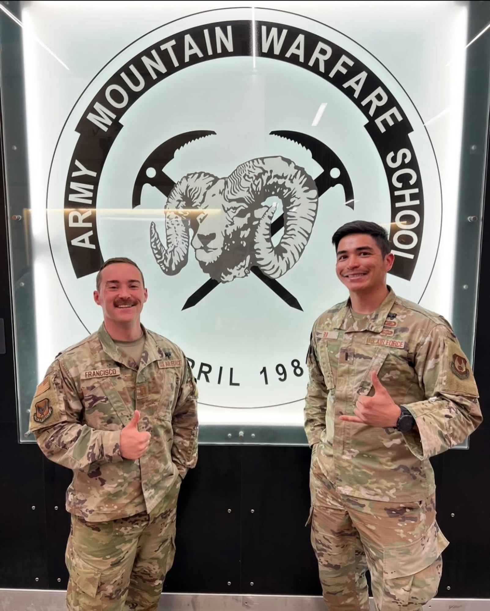 Two Airmen stand in front of school logo