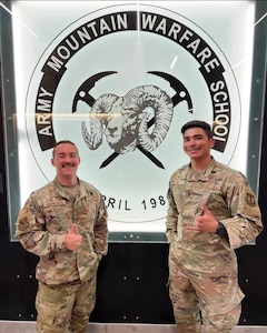 Two Airmen stand in front of school logo