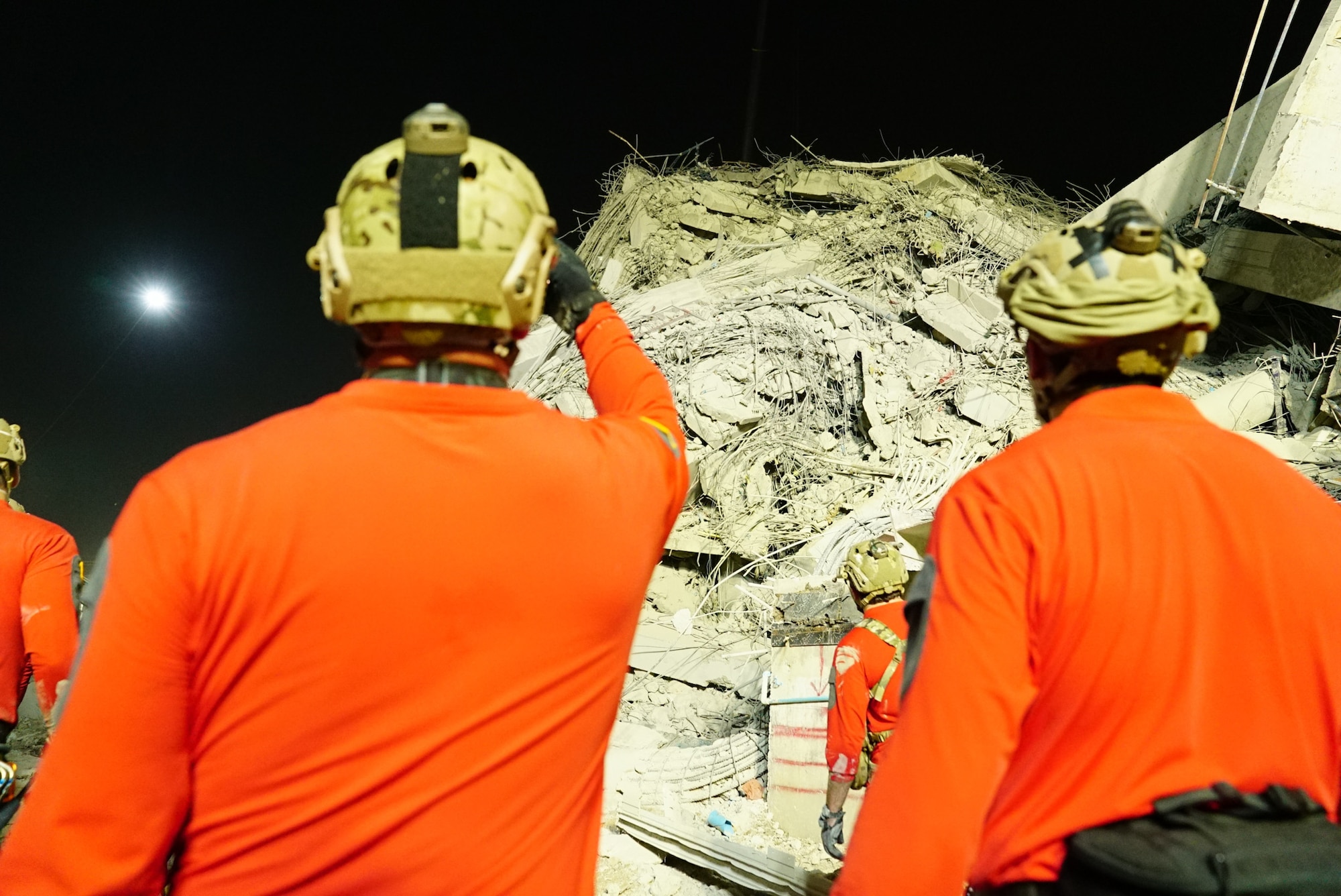Multiple military members look at a pile of rubble from a collapsed building.