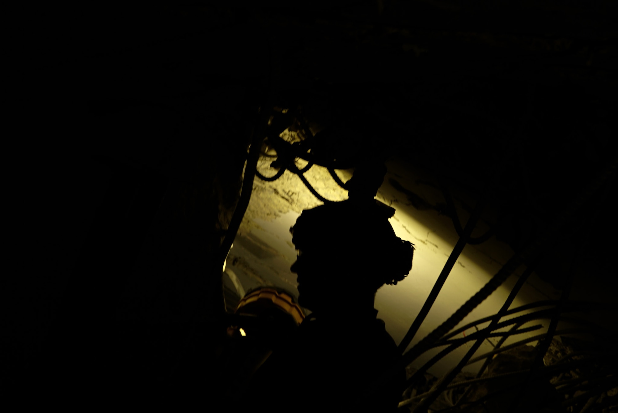 A military member uses his headlamp at night to search rubble of a fallen building.