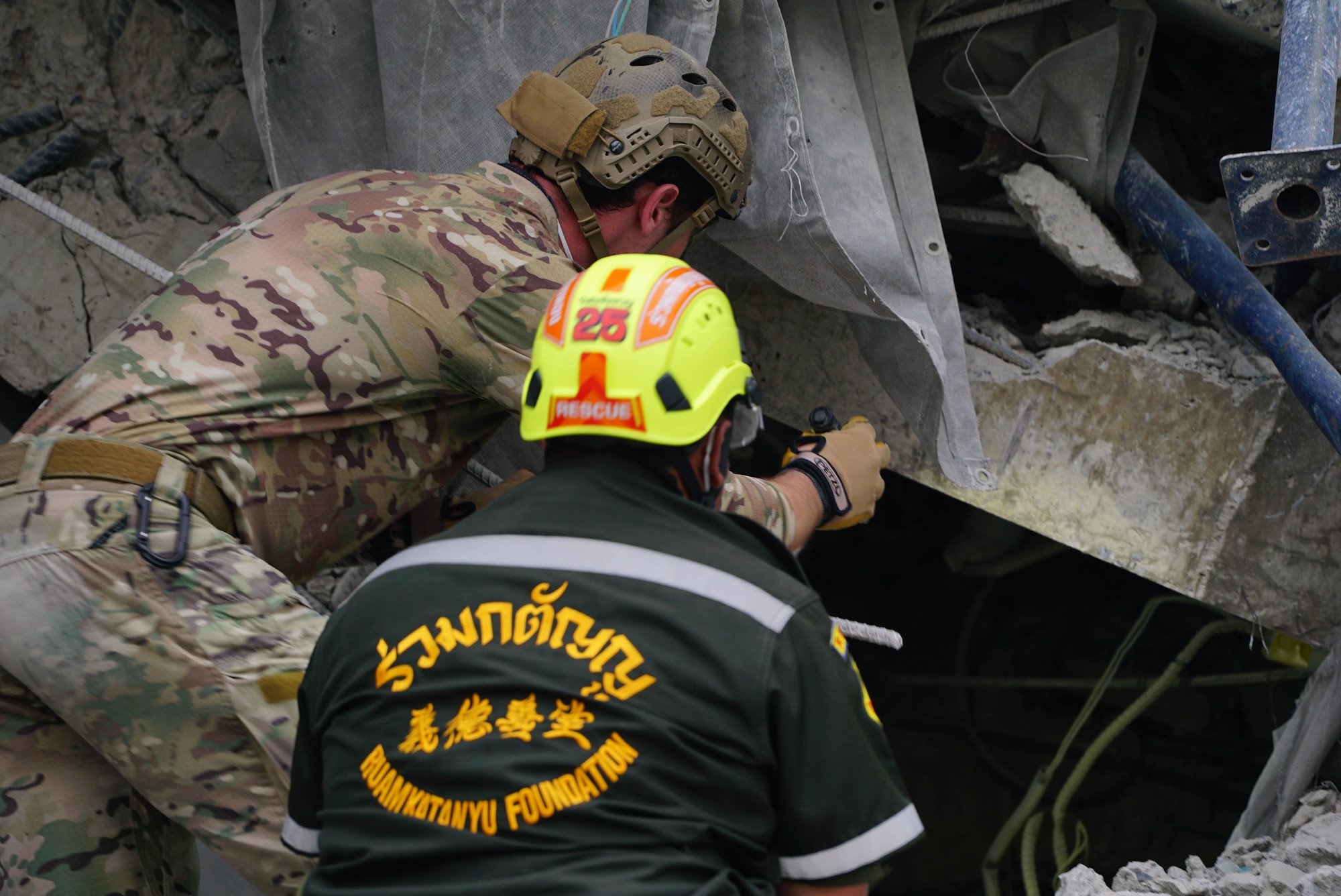 Two men look underneath rubble from a collapsed building.