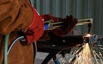 a torch is held by two hands wearing protective clothing. the torch is being used to cut metal