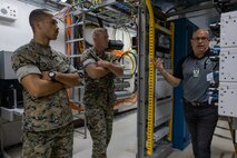Two Marines strand with arms crossed as a contractor technician explains work going on with a telecomminication system.