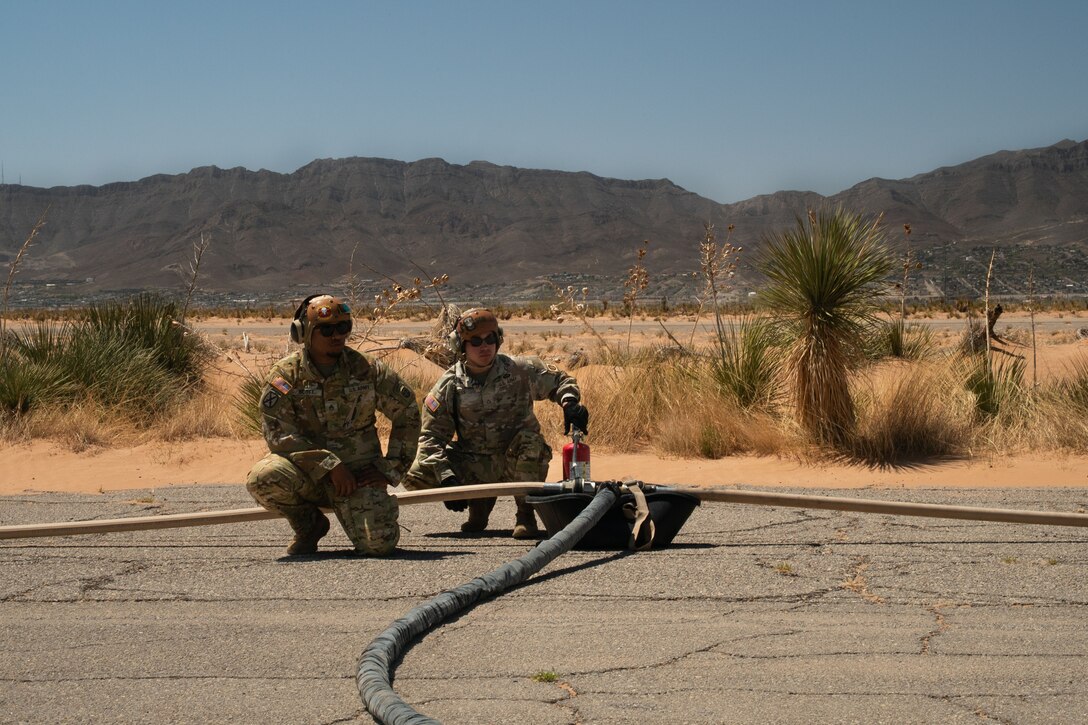 Two soldiers watch over three hoses during a refueling operation.