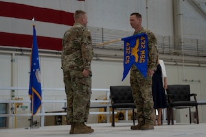 Two airmen stand facing each other while a guidon flag separates them.
