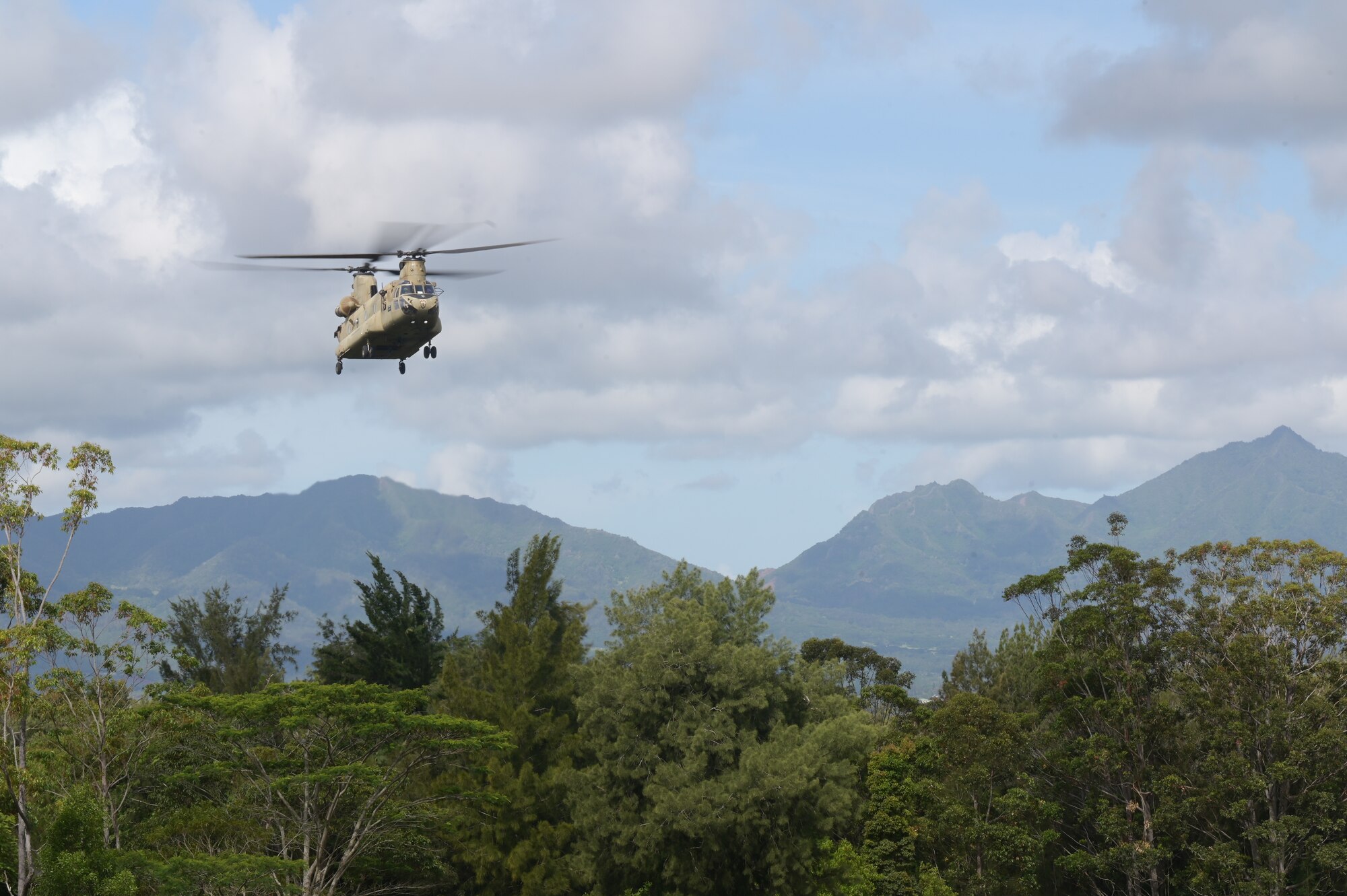 A chinook flying in the sky with a mountain in the backdrop.