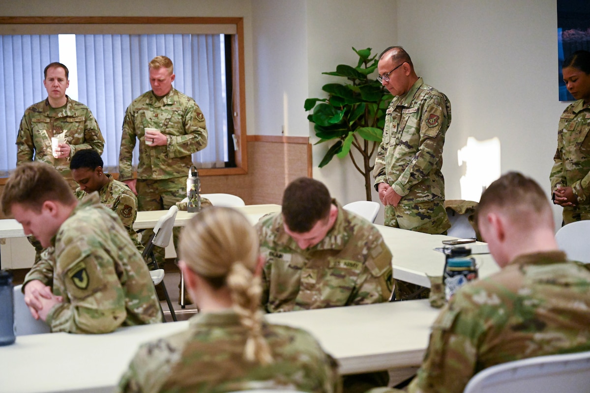 Several service members bow their heads across a room.