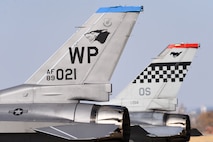 Two F-16 tails are shown side-by-side, one with a 8th Fighter Wing "Wolf Pack" logo and one with a 51st Fighter Wing "Mustang" logo.