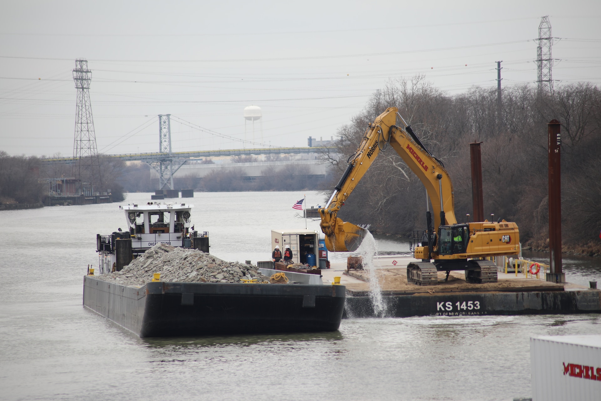 A contractor working on the Brandon Road Interbasin Project uses an excavator on a barge to gather broken bedrock from the bottom of the Illinois Waterway and place it on another barge for removal from the site.