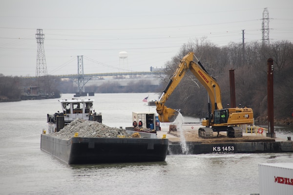 A contractor working on the Brandon Road Interbasin Project uses an excavator on a barge to gather broken bedrock from the bottom of the Illinois Waterway and place it on another barge for removal from the site.