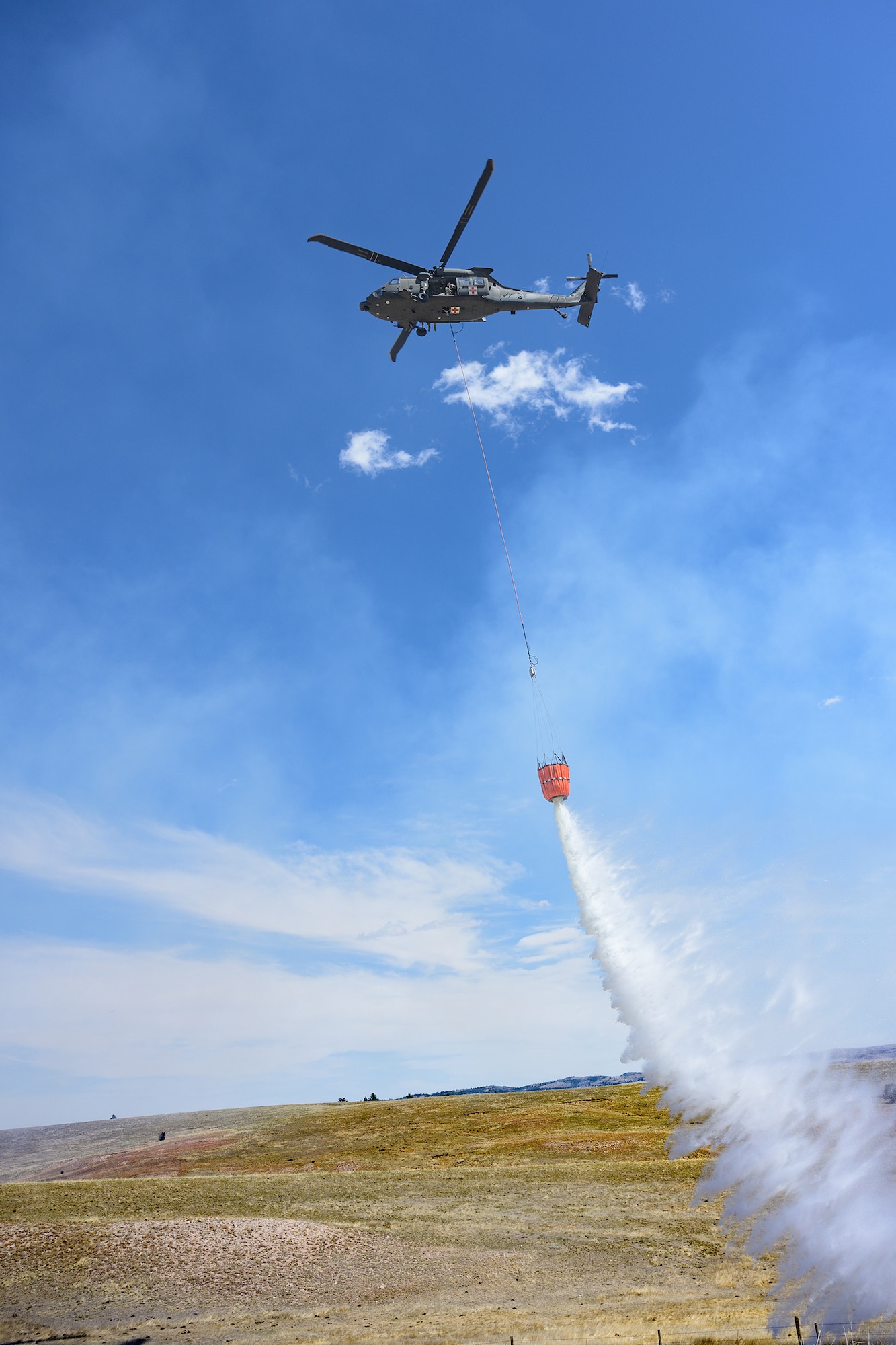 A HH-60M Black Hawk, assigned to Wyoming Army Aviation Support Facility, releases water during an interagency bucket drop training at Camp Guernsey, Wyoming, on April 16, 2025.