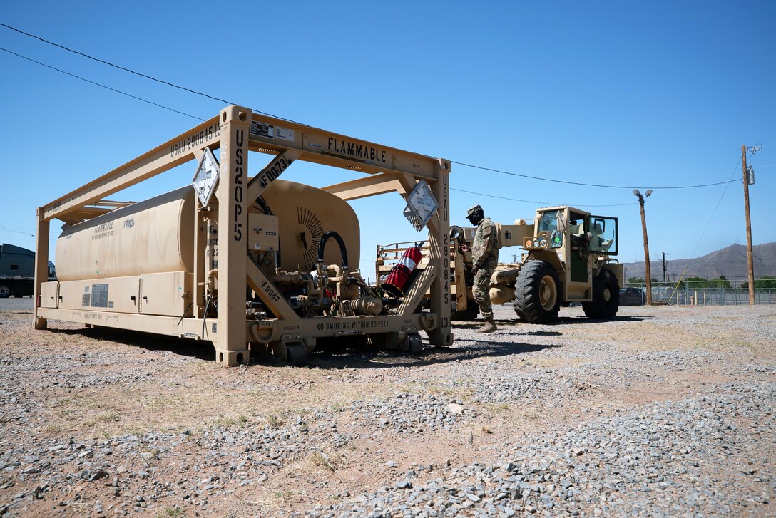 A soldier directs a tractor as it prepares to move a large piece of equipment on a gravel road.