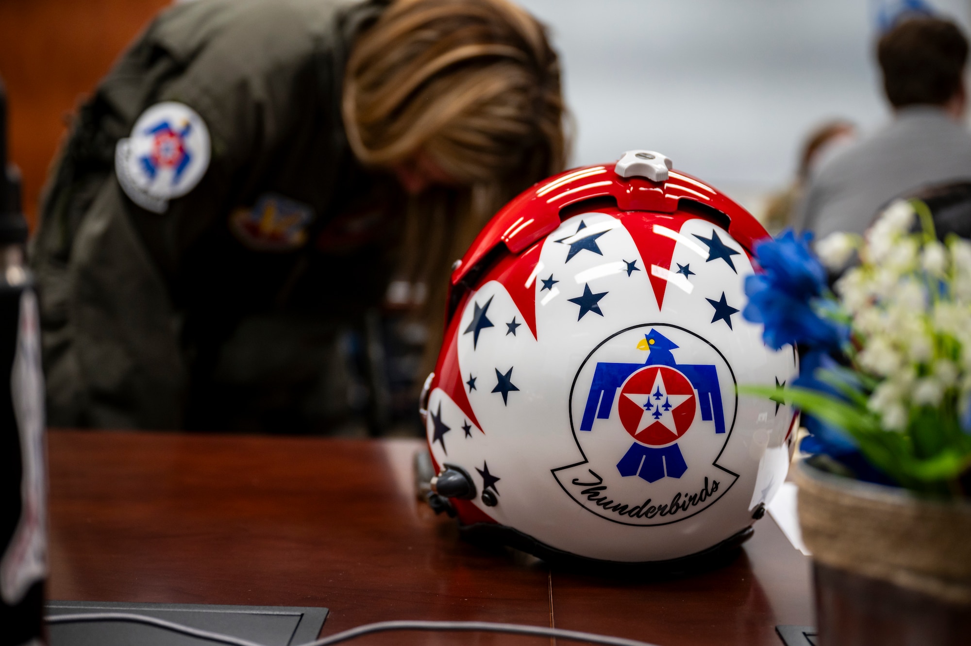 A helmet from the U.S. Air Force Air Demonstration Squadron "Thunderbirds" sits on a table while Cari Selzer, Hometown Hero participant, equips a G-suit before an incentive flight at Dyess Air Force Base, Texas, April 18, 2025. Selzer is a dedicated nurse practitioner with 30 years of experience. Her unwavering commitment to serving others, both locally and internationally, spans from life-saving emergency interventions, to consistent volunteer work, and nursing education. Her actions and career embodies the spirit of compassion and service. (U.S. Air Force photo by Staff Sgt. Leon Redfern)
