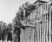 U.S. Army Corporal Larry Matinsk puts cigarettes into the extended hands of newly liberated prisoners behind a stockade in the Allach concentration camp, near Dachau Germany on April 30, 1945.