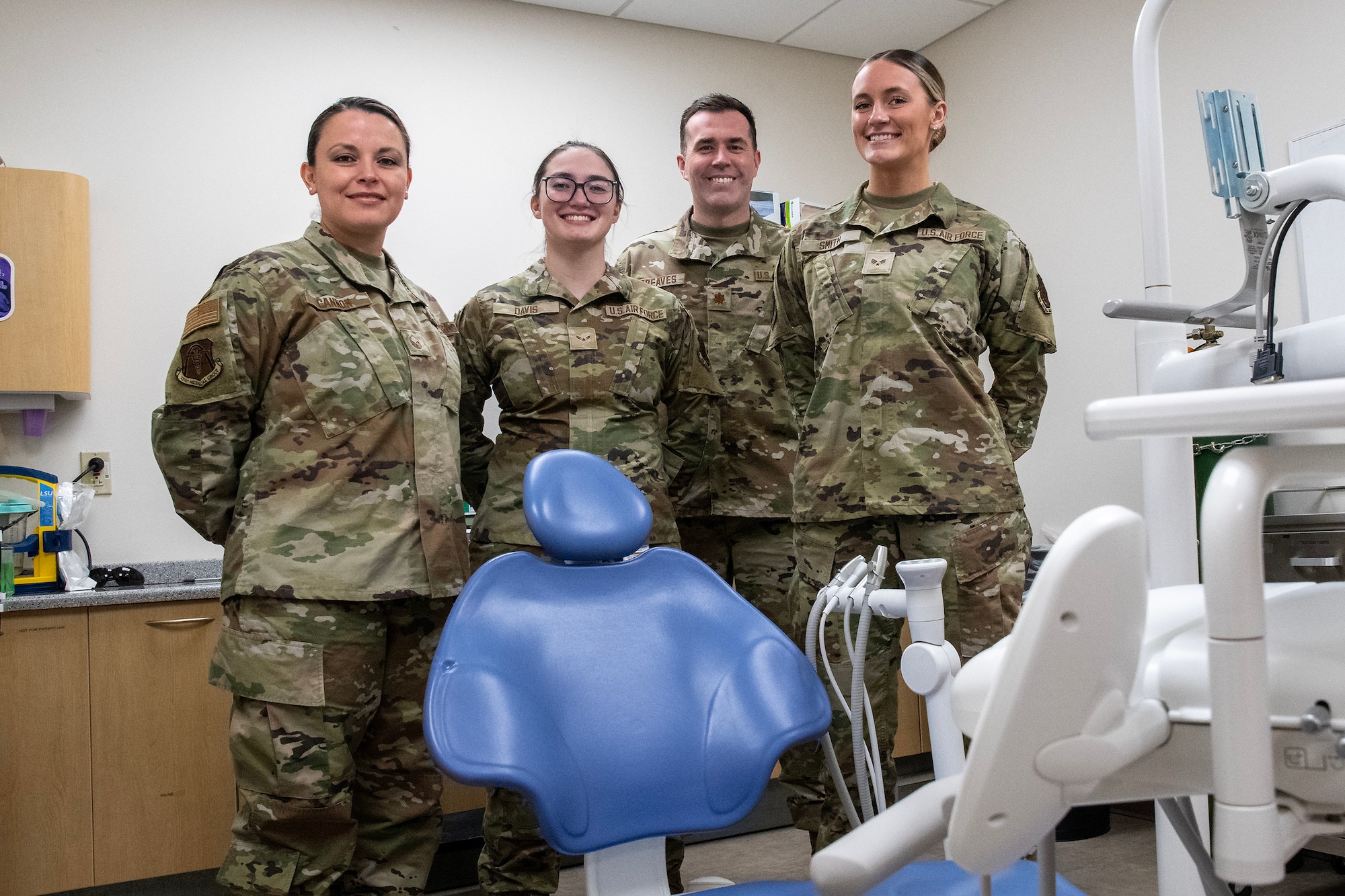 Four Air National Guard Airmen pose for a photo around a dentist's chair. The Airmen are wearing OCP pattern uniforms.