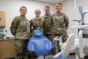 Four Air National Guard Airmen pose for a photo around a dentist's chair. The Airmen are wearing OCP pattern uniforms.