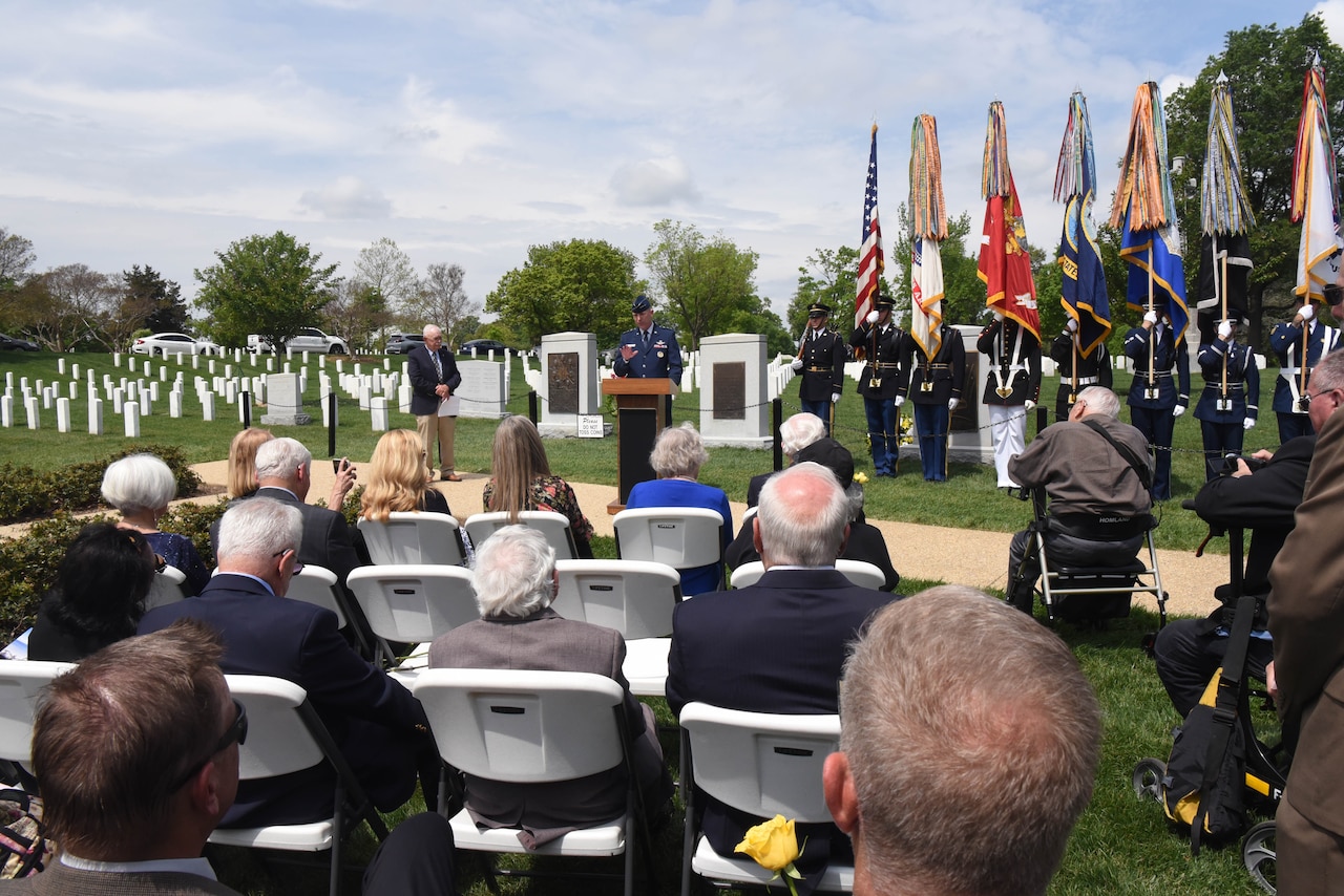 A man standing in a cemetery speaks to a seated crowd.