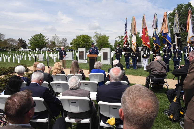 A man standing in a cemetery speaks to a seated crowd.
